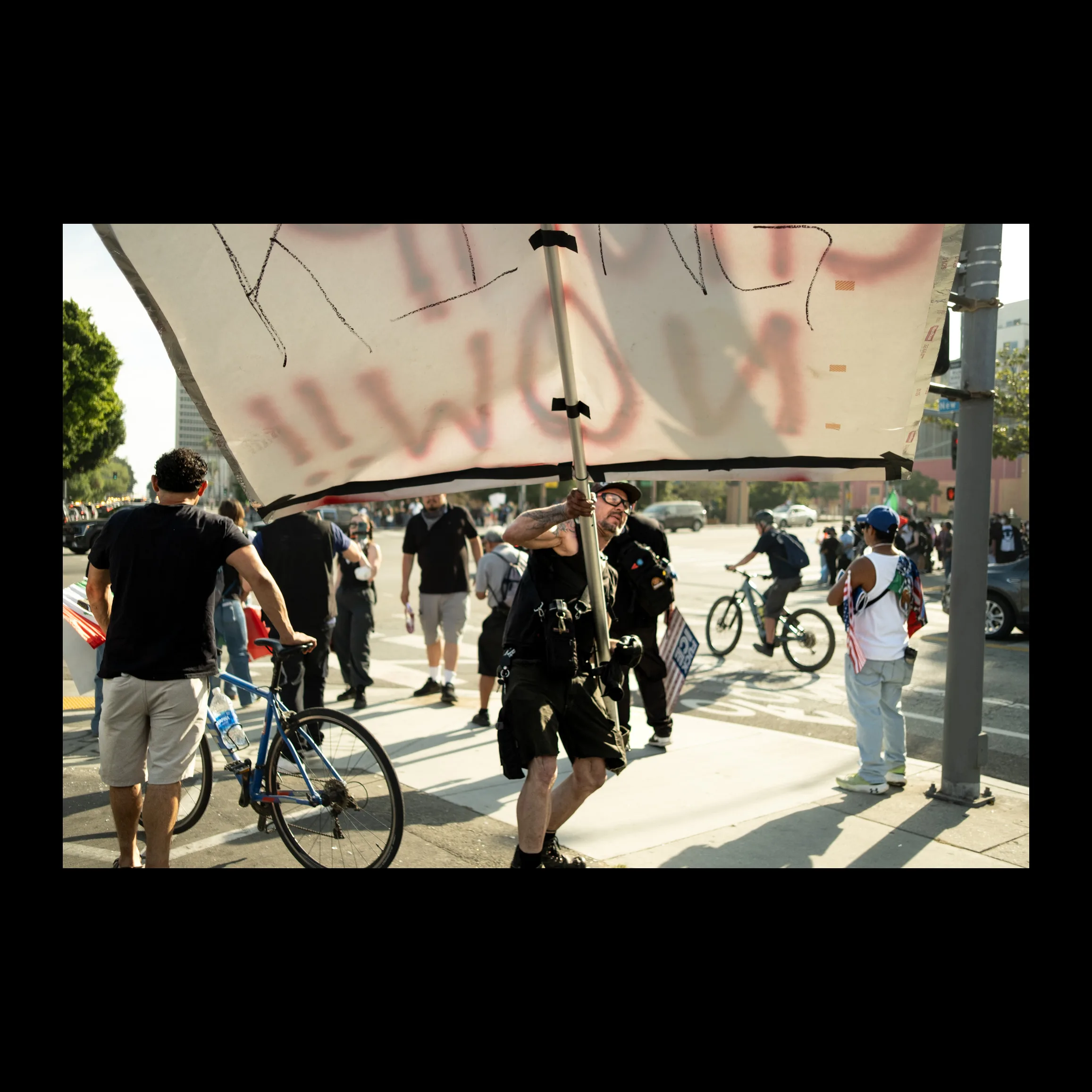 Protester hoisting a large spray-painted banner in a plaza as cyclists gather