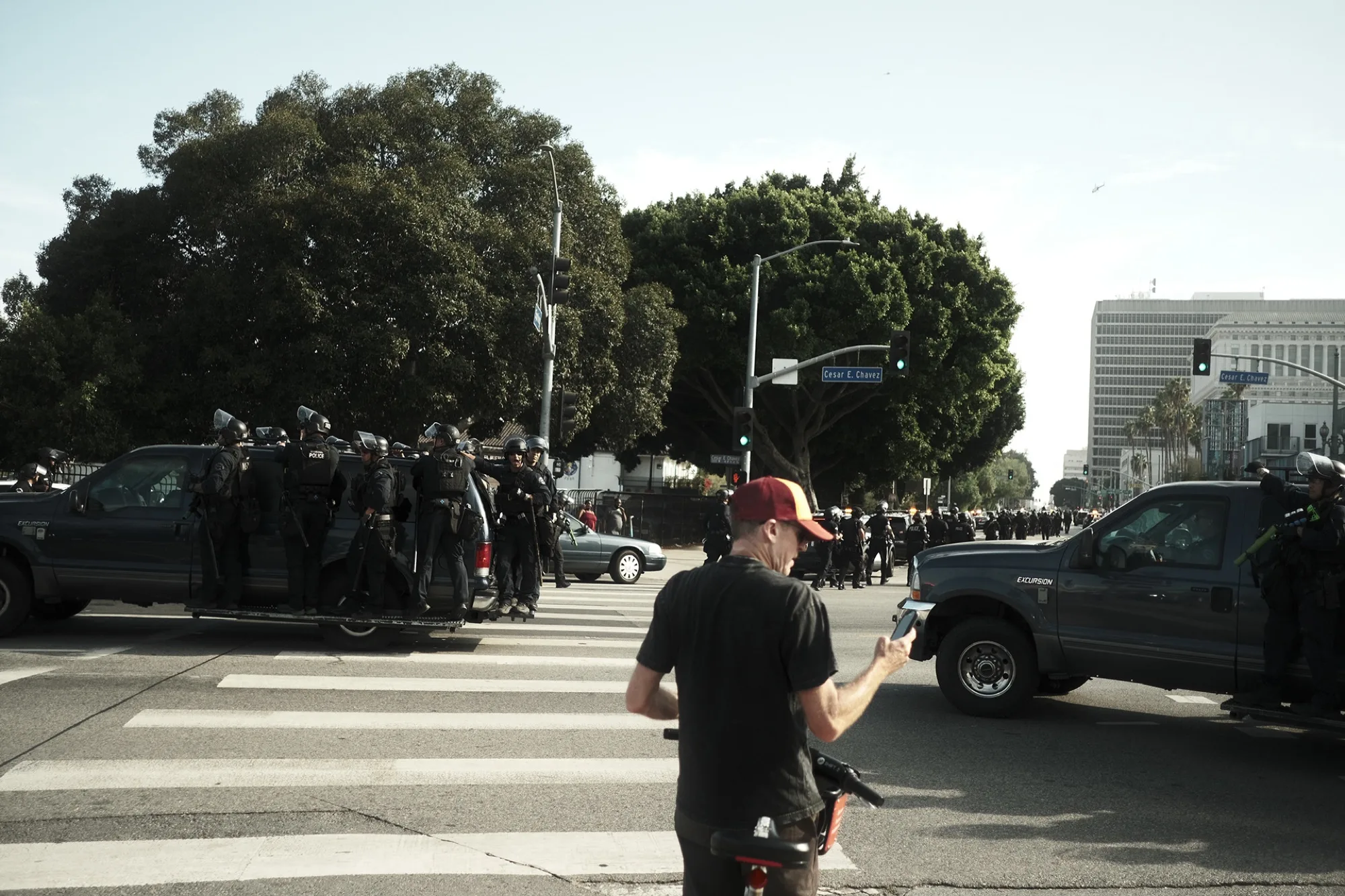 Man in a red cap at a crosswalk between police trucks and an assembled riot line