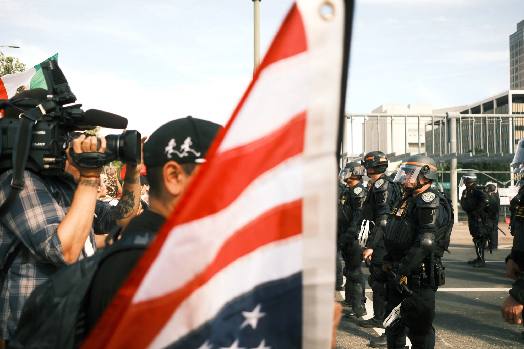 American flag in the foreground as a cameraman films a line of riot police