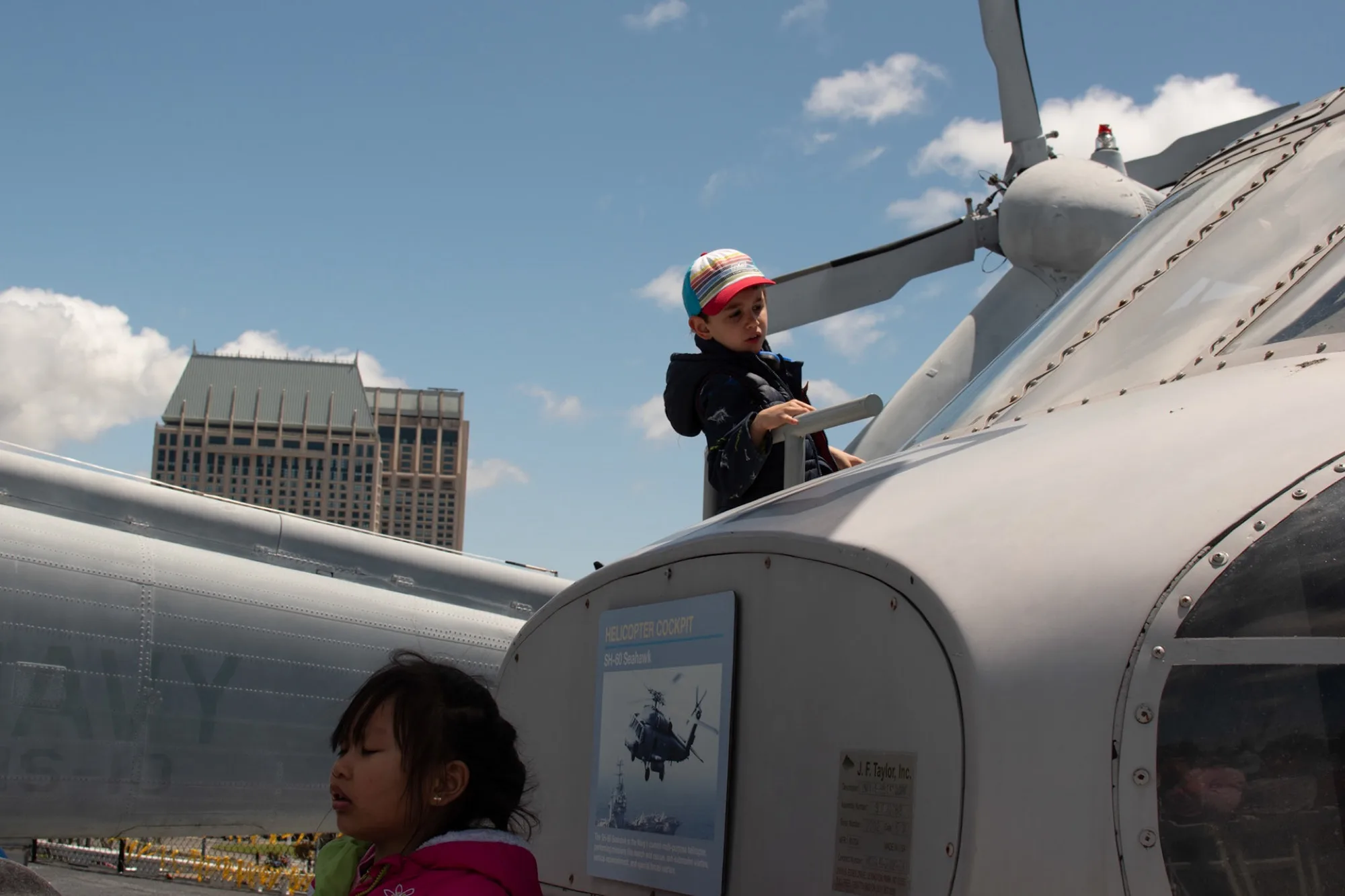 Children climbing on a museum Navy helicopter, a high-rise in the background