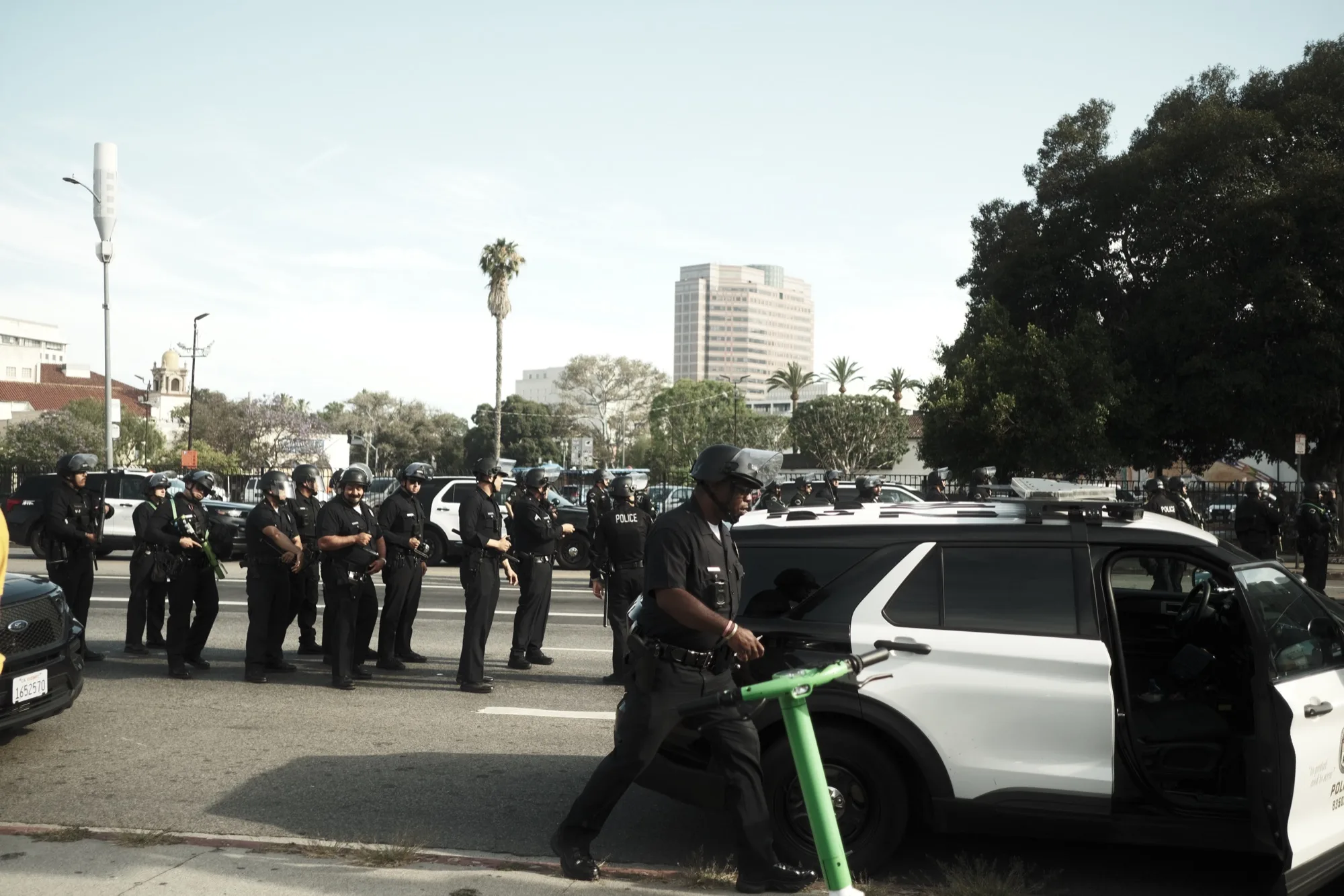 Police line along a boulevard as an officer wheels a green rental scooter