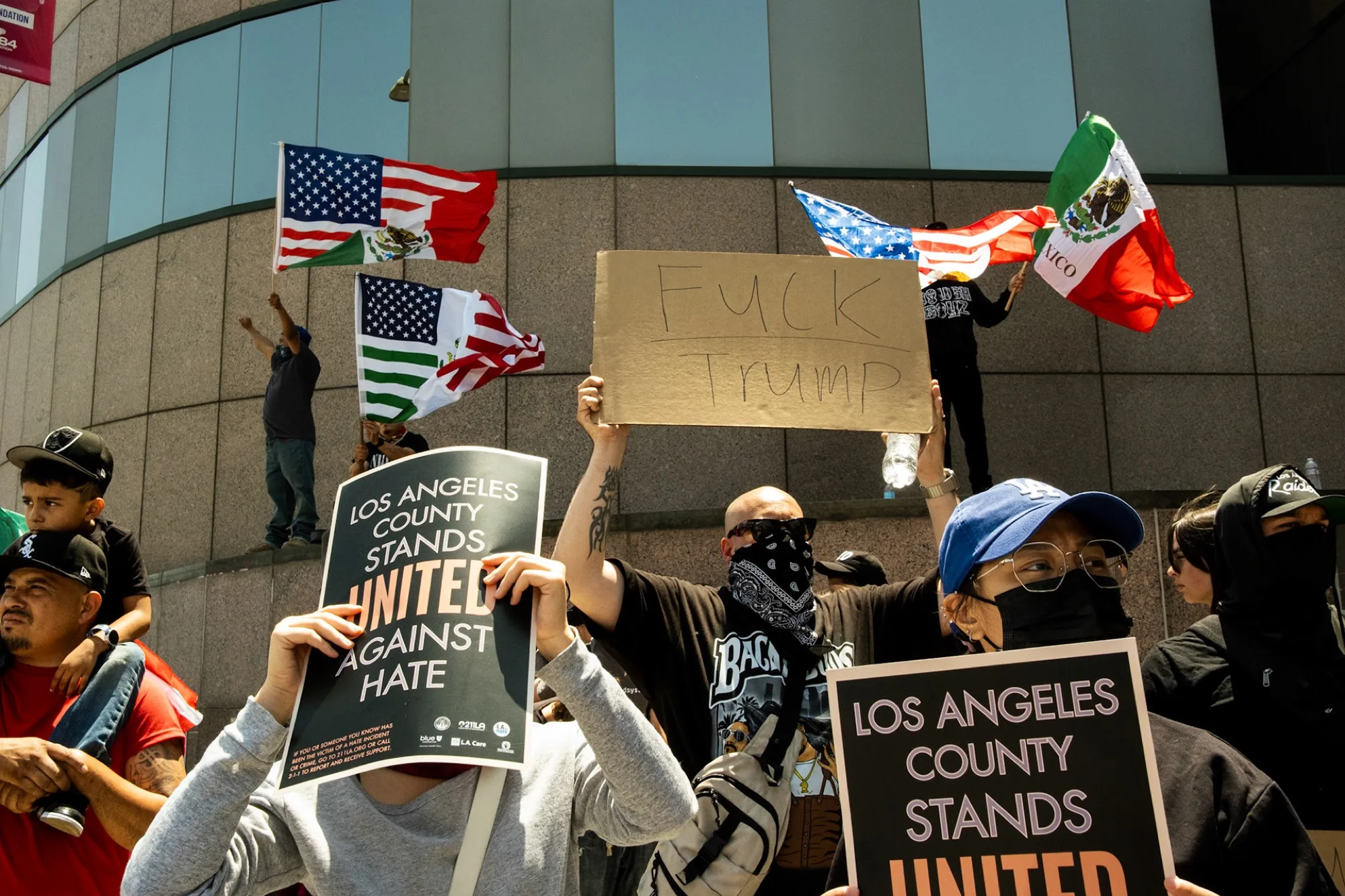 Crowd holding 'Los Angeles County Stands United Against Hate' signs with US and Mexican flags overhead